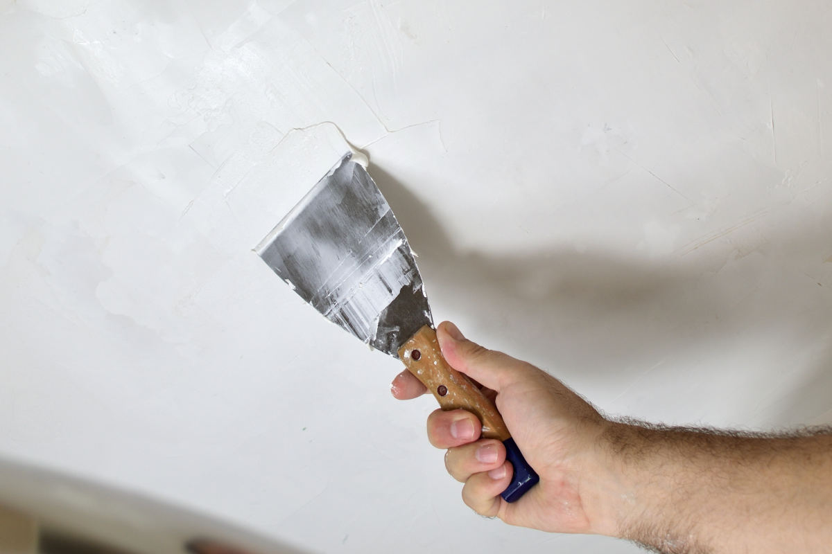 El maestro está aplicando masilla blanca en una pared y manchando con una  espátula en una sala de renovación de la casa durante el día